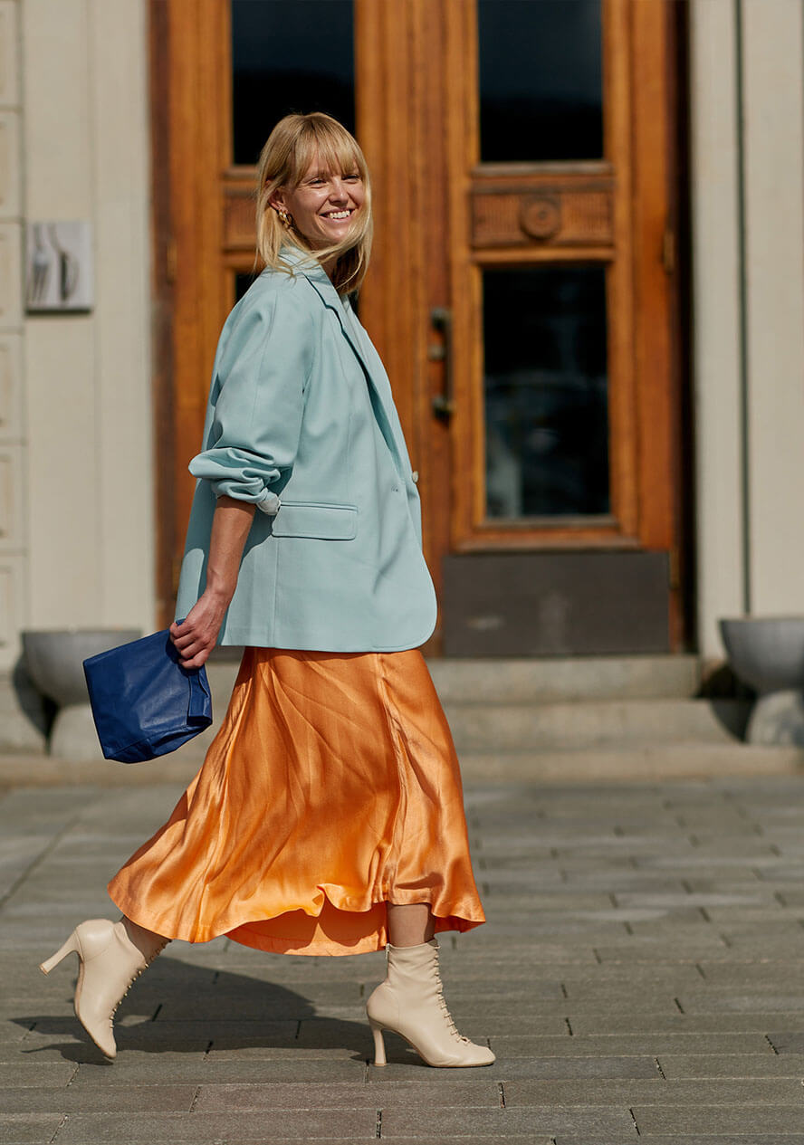 Frau trägt ein orangenes Satinkleid und kombiniert einen blauen Blazer als Color Blocking Look dazu