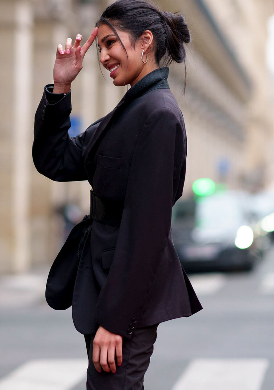 Frau trägt einen schwarzen Blazer und schwarze Hose und kombiniert einen Gürtel dazu