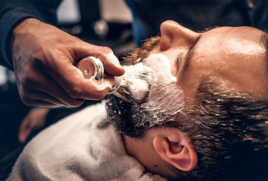 Mann bekommt Bart mit Pinsel und Rasierschaum rasiert