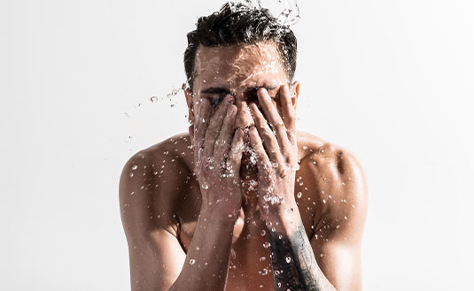 Mann mit dunklen Haaren wäscht sein Gesicht mit Wasser