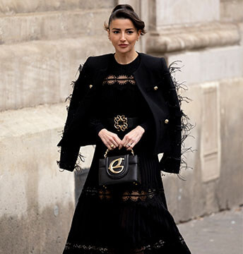 Brünette Frau mit schwarzem, bodenlangen Kleid, schwarzer Clutch und schwarzer Jacke