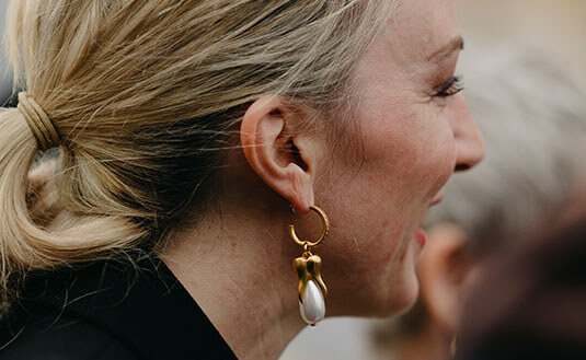 Blonde Frau mit Zopf trägt mit Gold besetzte Perlenohrringe