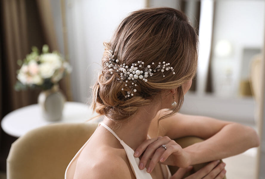 Braut vor einem Spiegel mit Hochsteckfrisur und Blüten im Haar