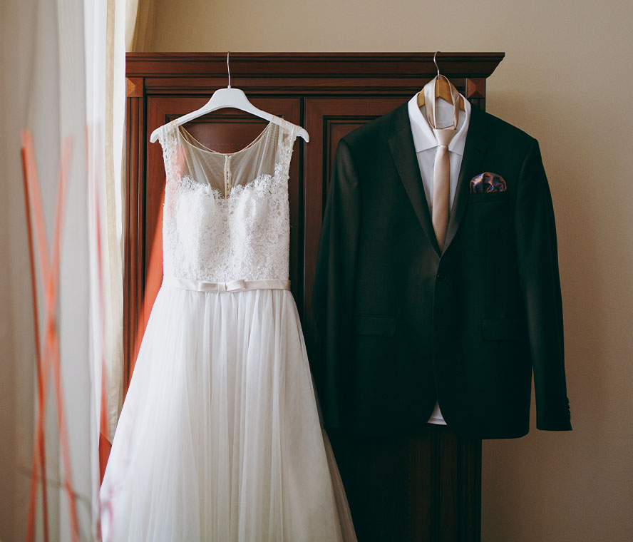 Brautkleid und Hochzeitsanzug hängen an einem Schrank