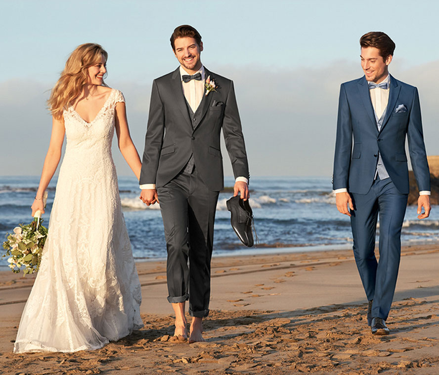 Zwei Männer in blauem und grauem Hochzeitsanzug und eine Braut am Strand