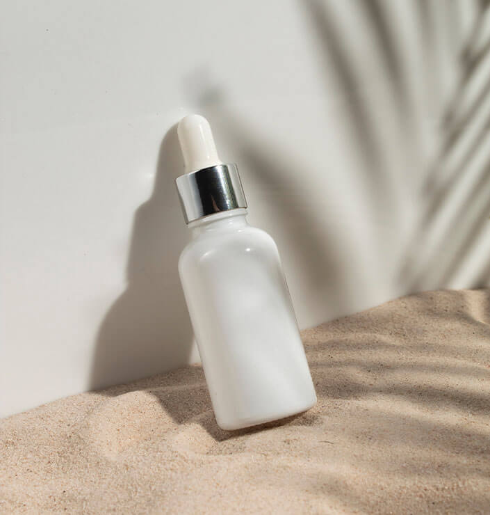 Weiße Kosmetikflasche im Sand angelehnt an eine Wand