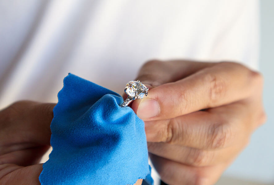 Frau poliert einen Diamantring mit einem Mikrofasertuch