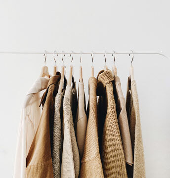 Beiger Mantel, Pullover, Bluse und weitere Kleidung auf einer Kleiderstange