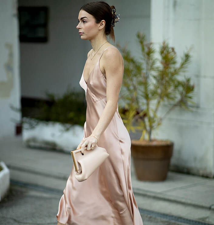 Brünette Frau in einem eleganten Outfit mit pastellrosa Slipdress, Slingpumps und Clutch
