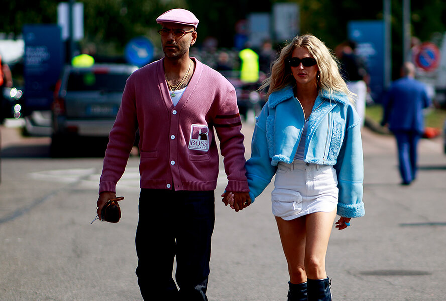 Mann mit rosa Cardigan und rosa Mütze und Frau in weissem Mini-Rock und blauer Felljacke tragen den Y2K-Look
