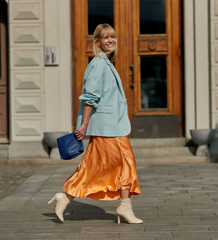 Frau in einem orangenen Seidenrock mit blauem Blazer als Business Casual Look