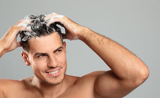 Mann mit dunklen Haaren schamponiert sich das Haar