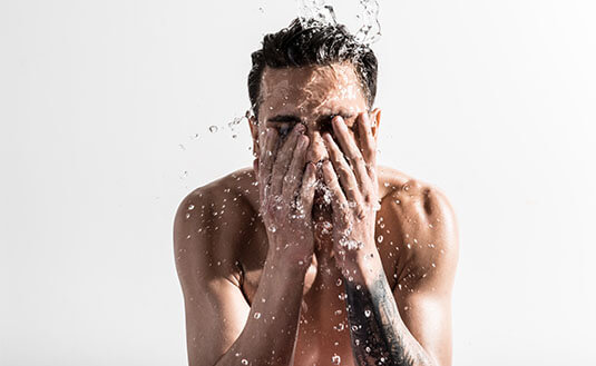 Mann mit dunklen Haaren wäscht sein Gesicht mit Wasser