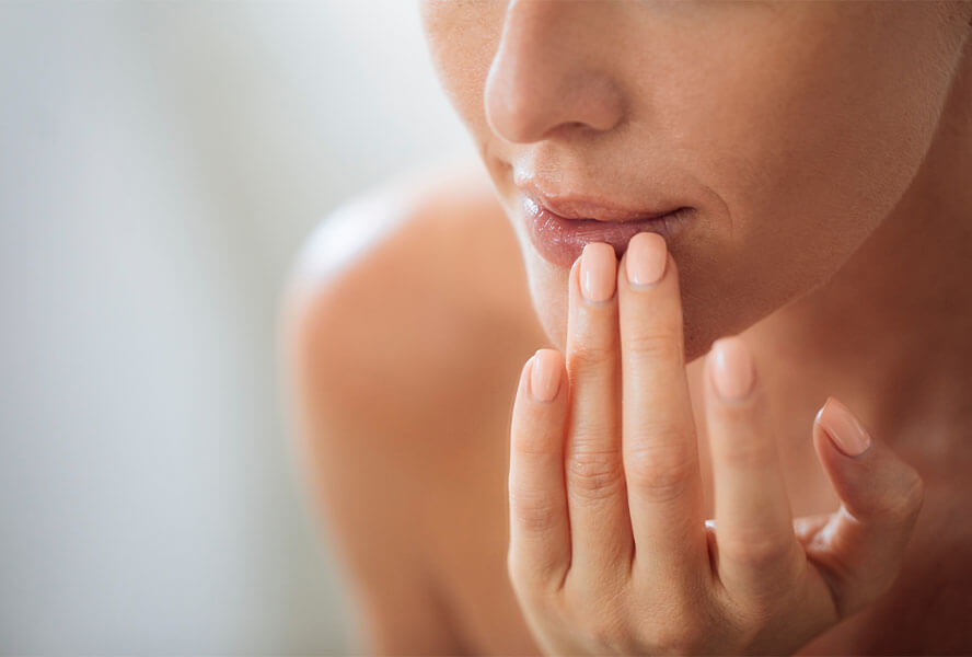 Frau mit cremefarbenem Nagellack betastet vorsichtig ihre Lippen
