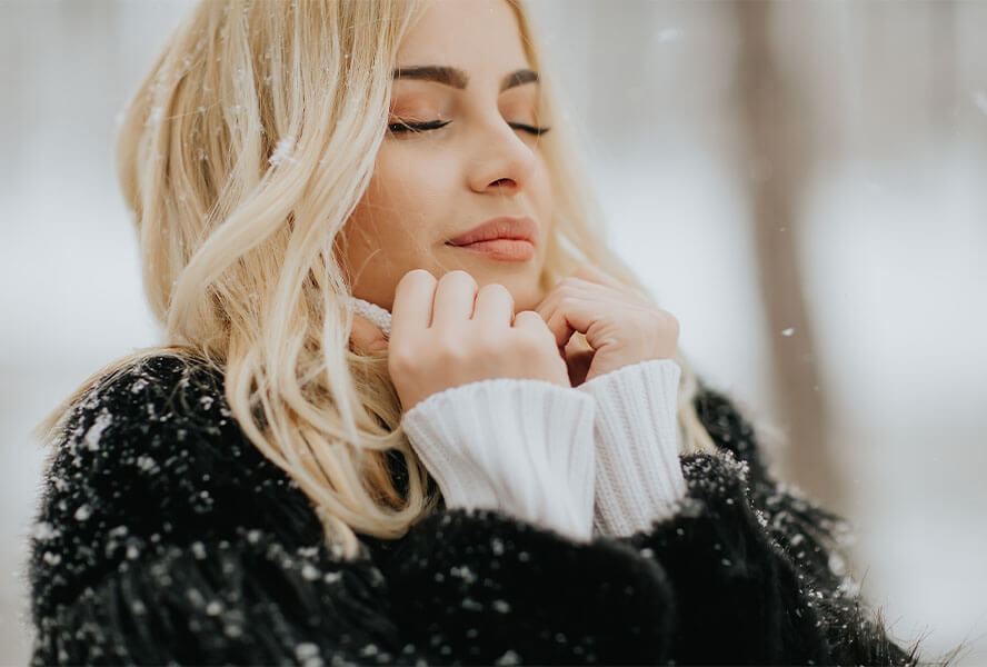 Blonde Frau mit schwarzer Jacke im Winter mit Schneeflocken im Haar