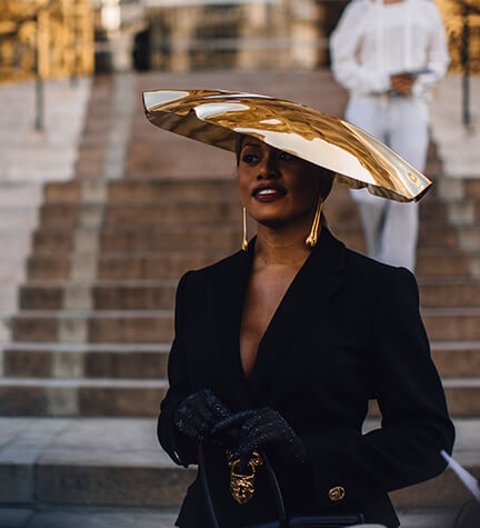 Frau in schwarzem Blazer mit goldenem Hut als Hochzeitsgast