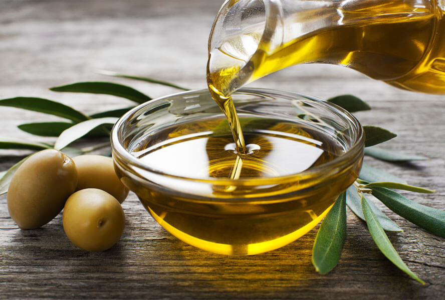 Olivenöl wird in ein Schälchen gegossen und drei grüne Oliven liegen daneben