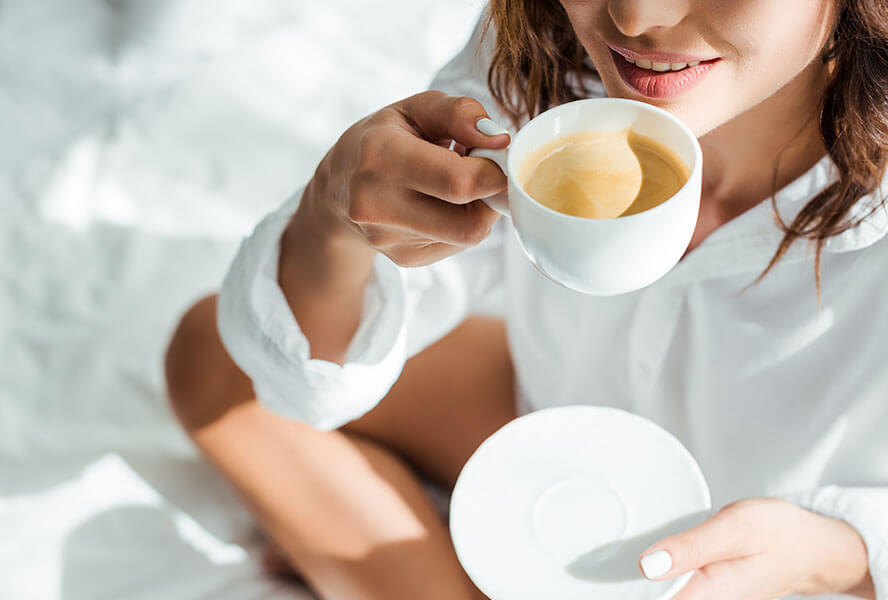 Frau sitzt im Bett und trinkt einen Kaffee