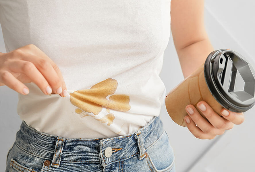 Frau verschüttet ihren Coffee to-go auf ihrem weissen Oberteil