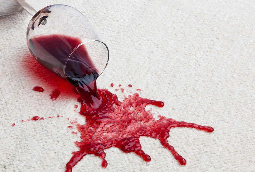 Ausgelaufenes Glas Rotwein auf cremefarbenem Teppich