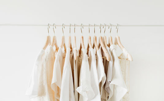 Weiße und cremefarbene Kleidungsstücke hängen auf einer Kleiderstange