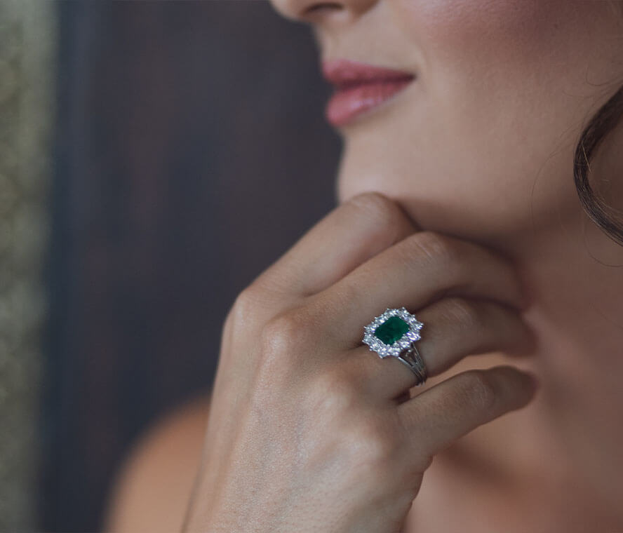 Frau trägt einen Edelsteinring mit einem Smaragdstein und Diamanten