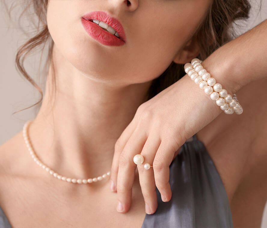 Frau trägt ein helles Set aus Perlenkette, Perlenarmband und Perlenring