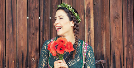 Lachende Frau mit braunen Haaren und geflochtenem Zopf trägt Dirndl und einen Blumenstrauß